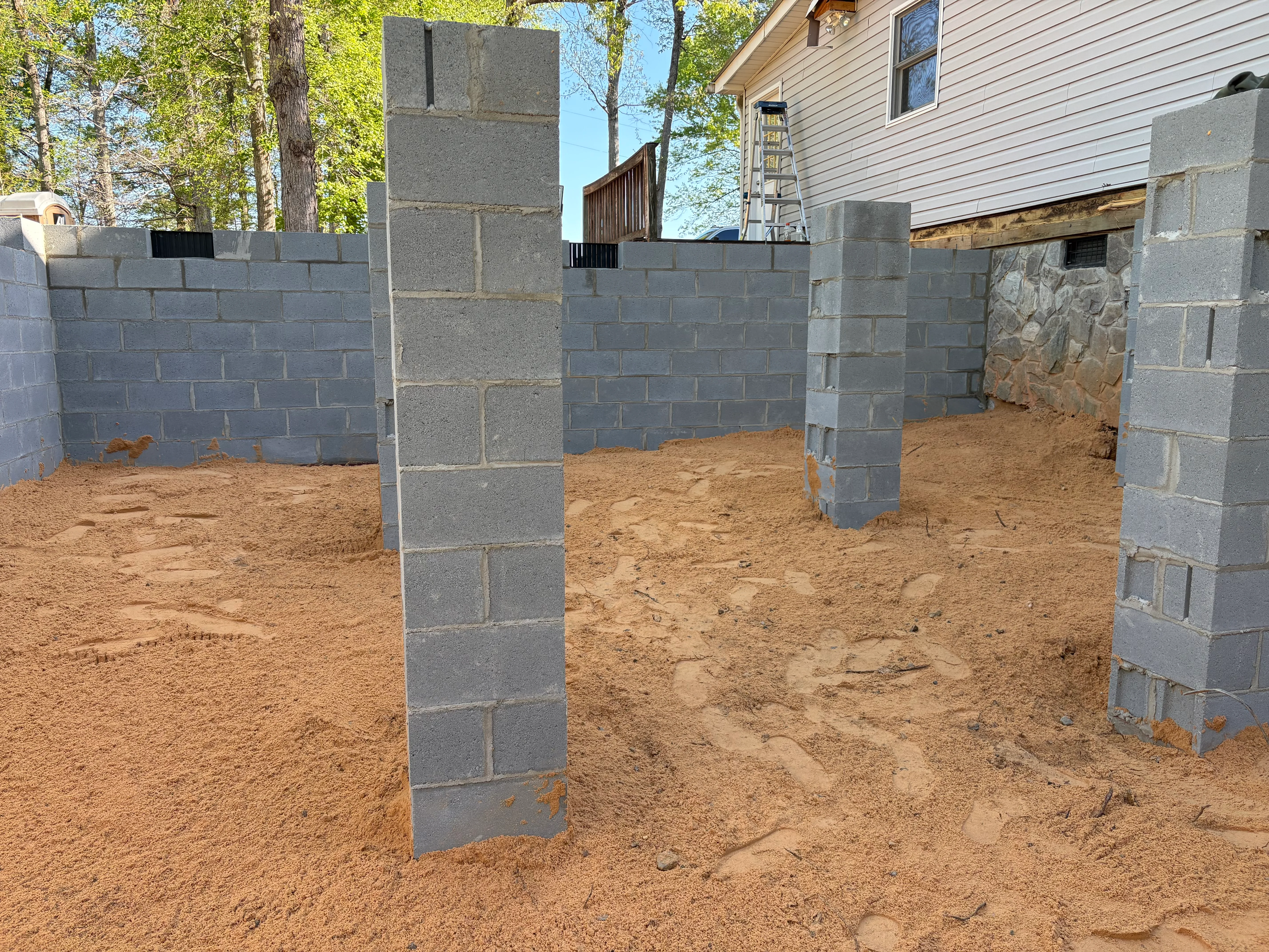 Concrete block foundation walls and support columns installed on brown soil base