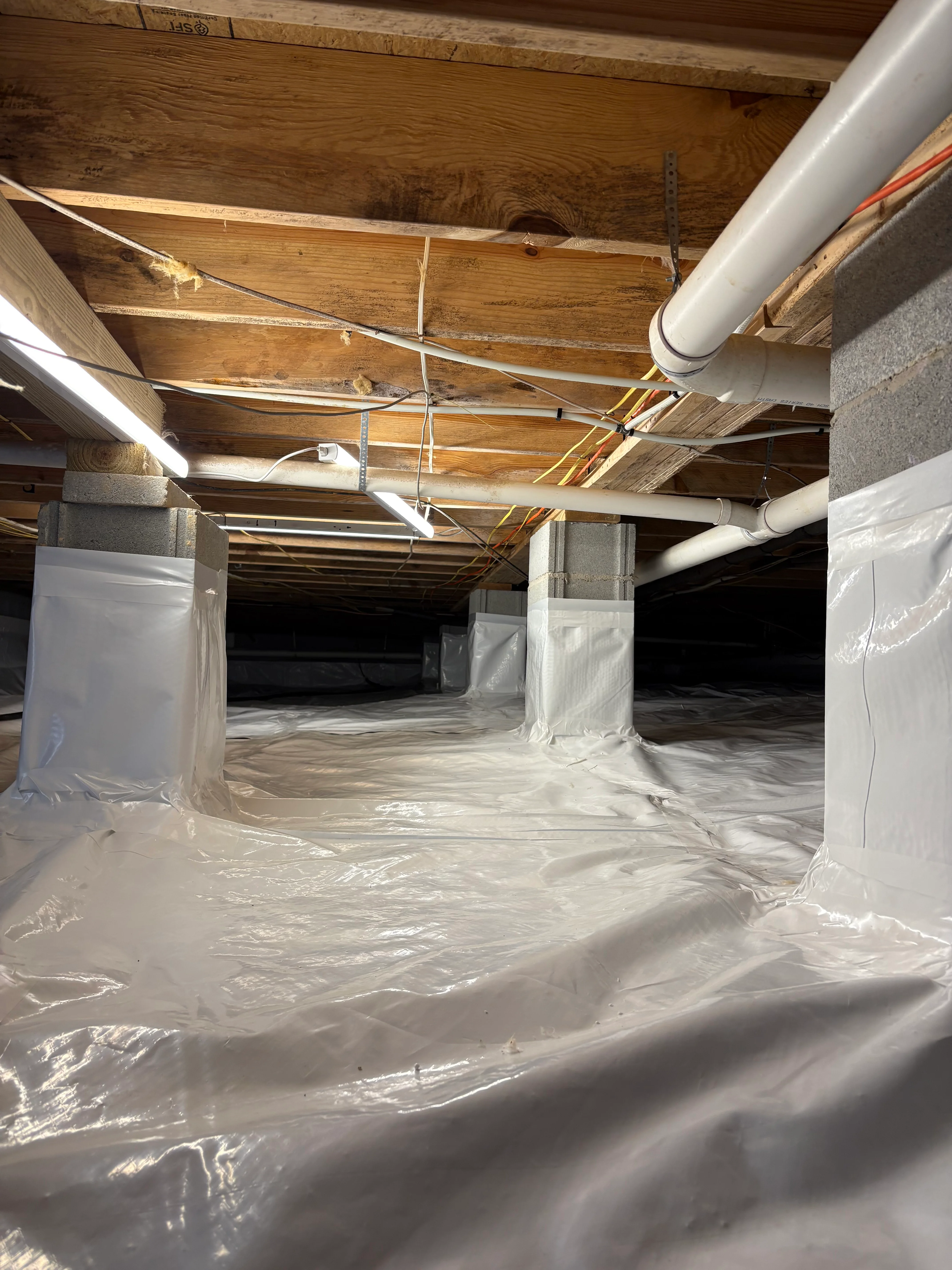 Crawl space with white vapor barrier covering floor and wrapped support columns