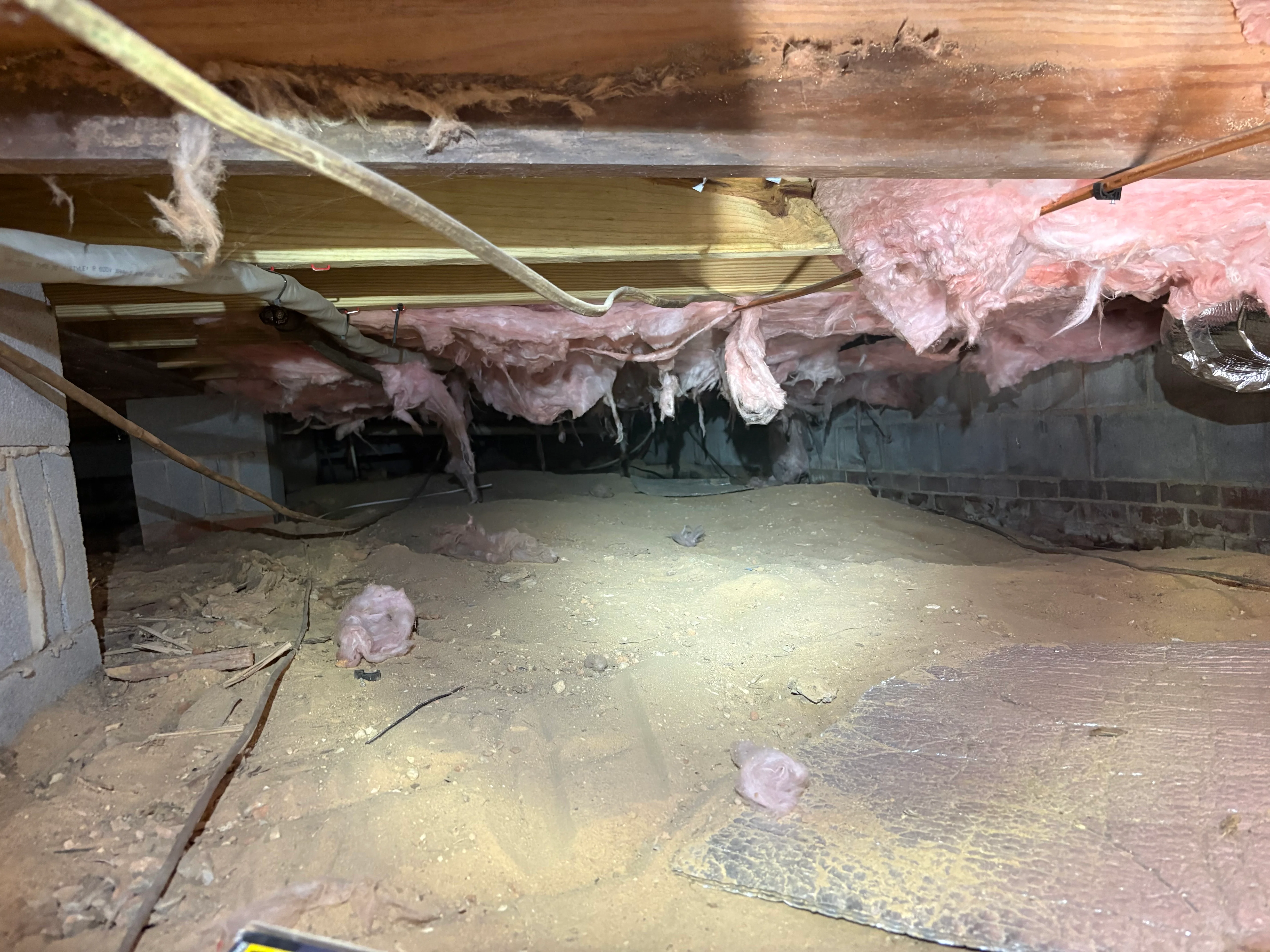 Crawl space with pink insulation batts and vapor barrier installed under wooden joists