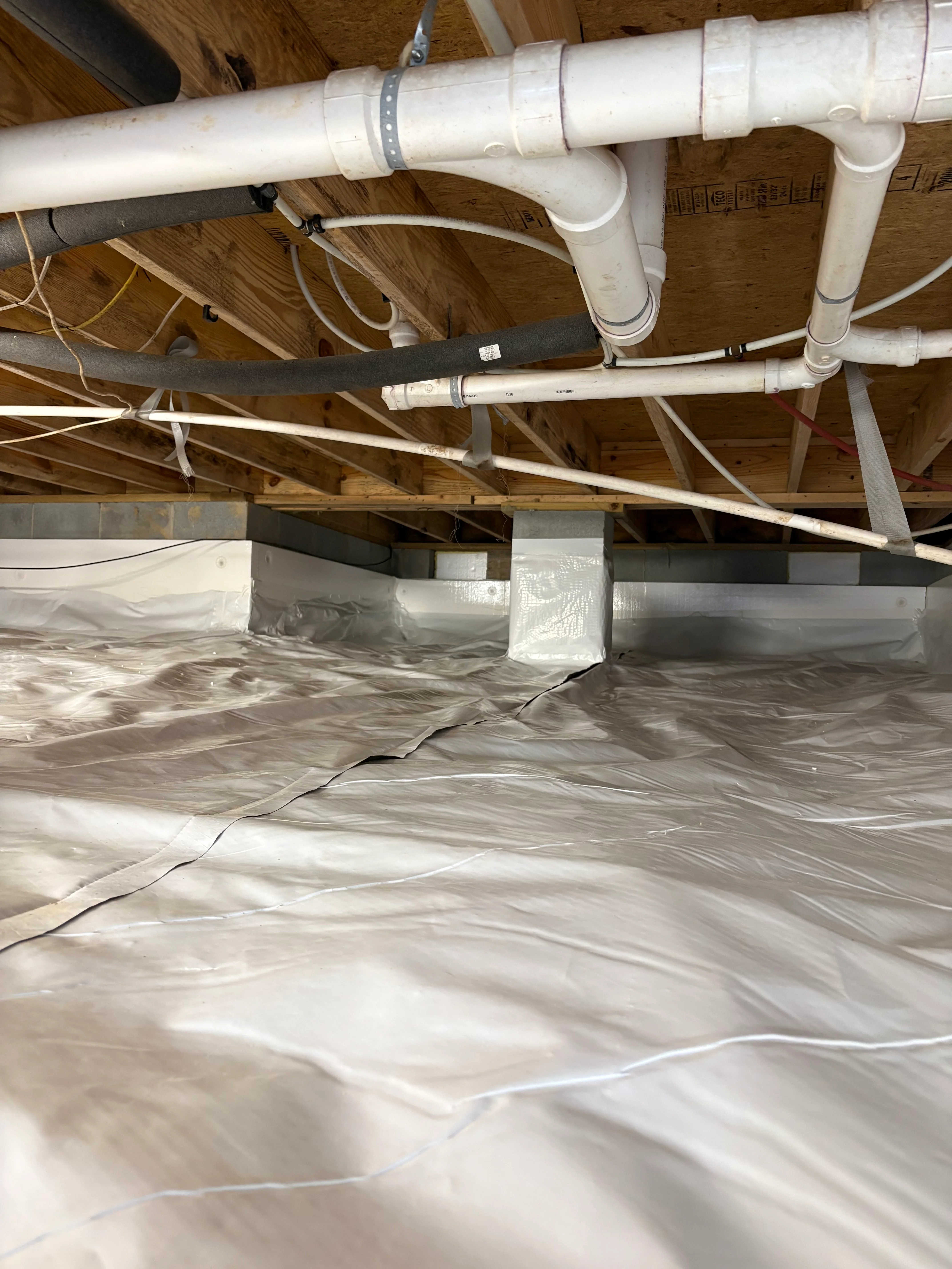 Crawl space with white vapor barrier, PVC piping, and moisture control system installed