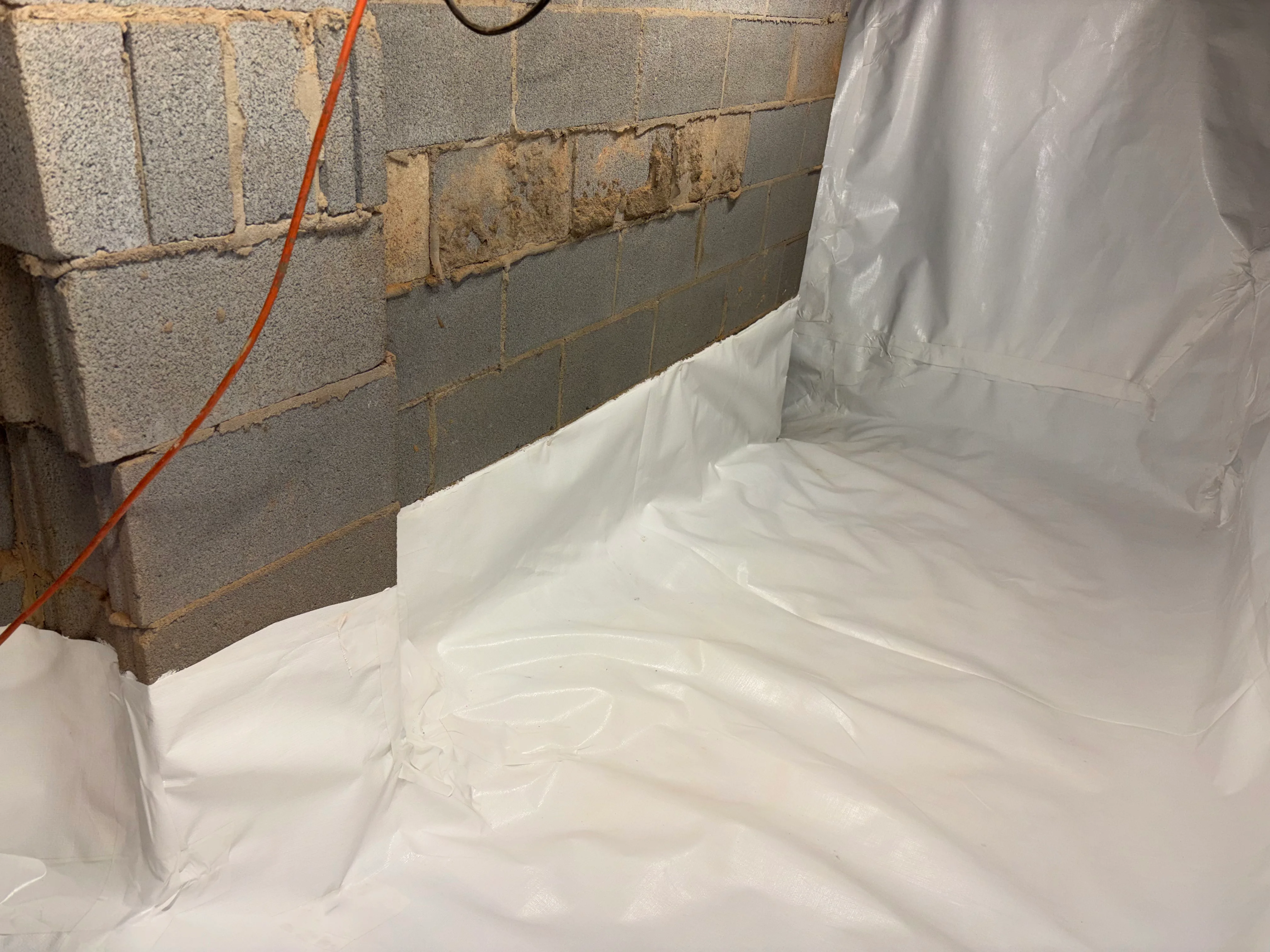 White vapor barrier installed on crawl space foundation walls with concrete block visible