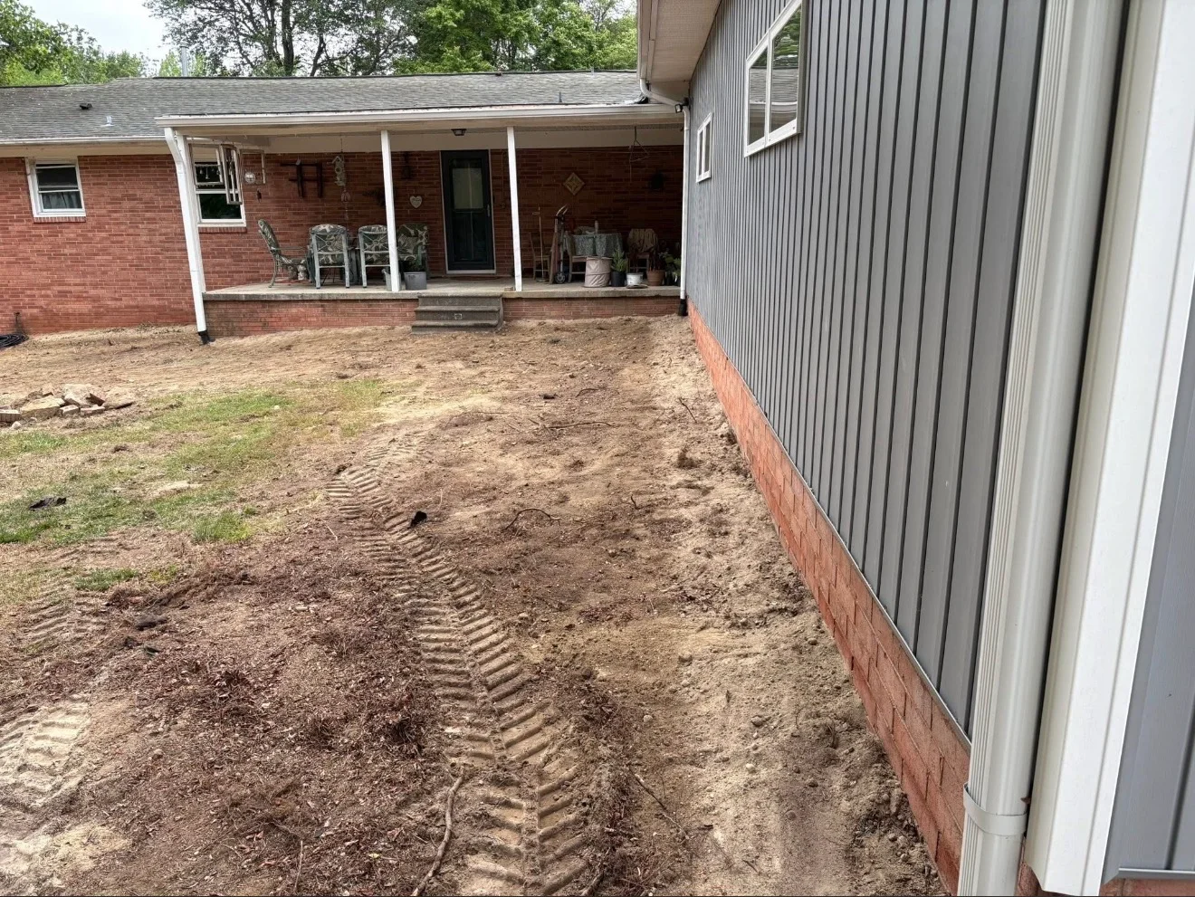 Excavated dirt yard with grading patterns around brick home foundation and metal shed