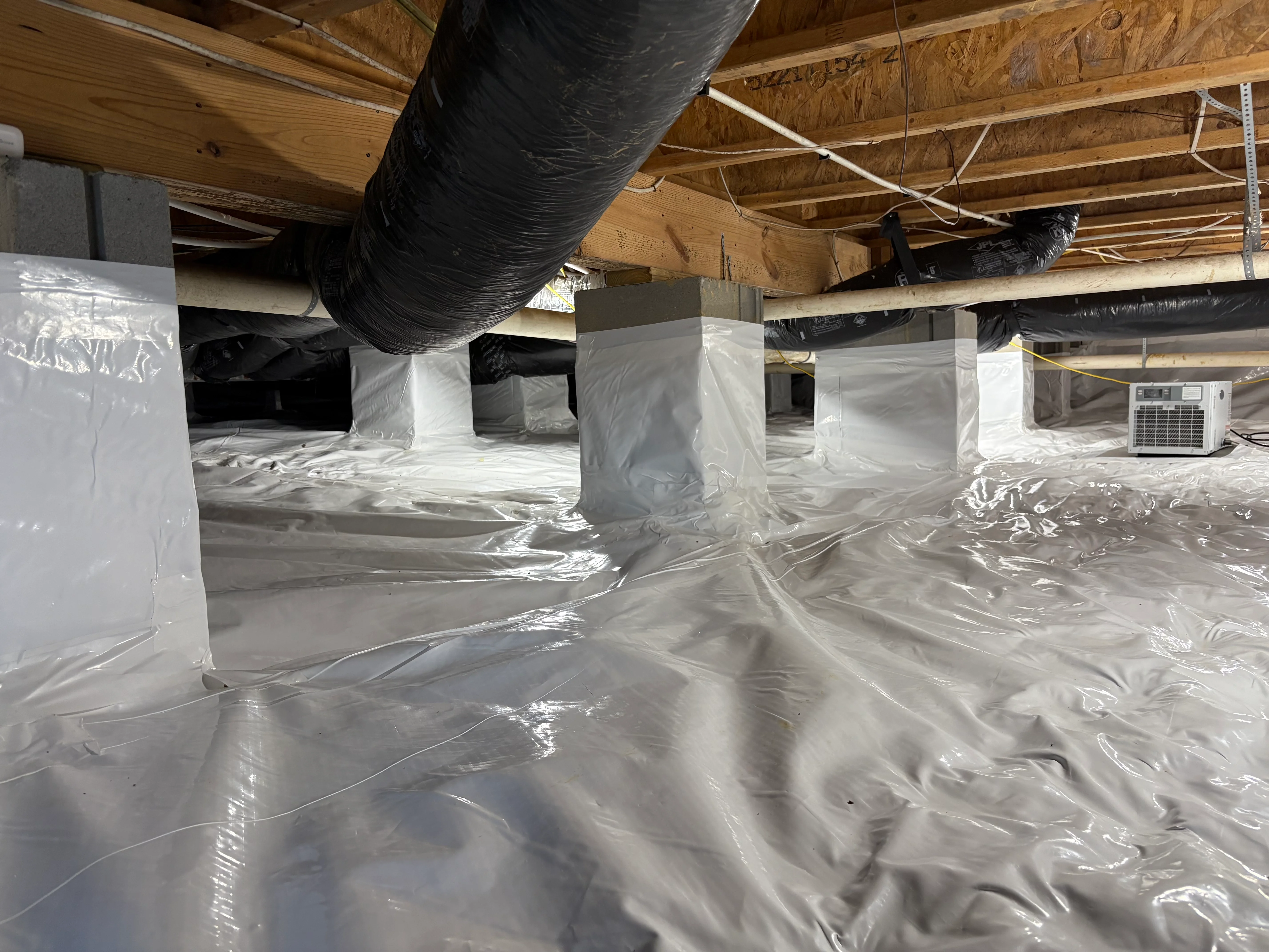 Crawl space with white vapor barrier encapsulation, support posts, and dehumidifier unit