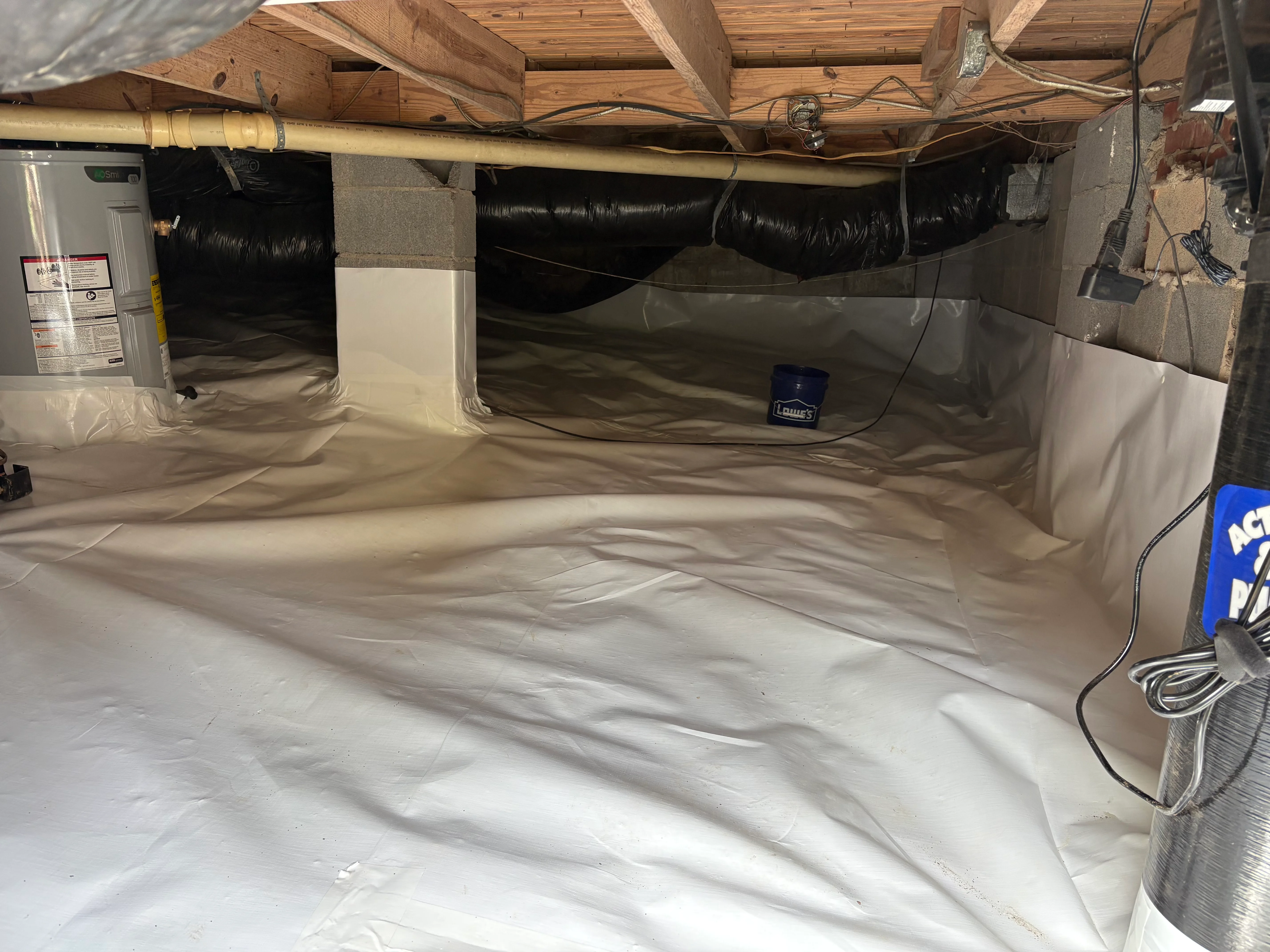Crawl space with white vapor barrier encapsulation, sealed seams, and drainage system installed