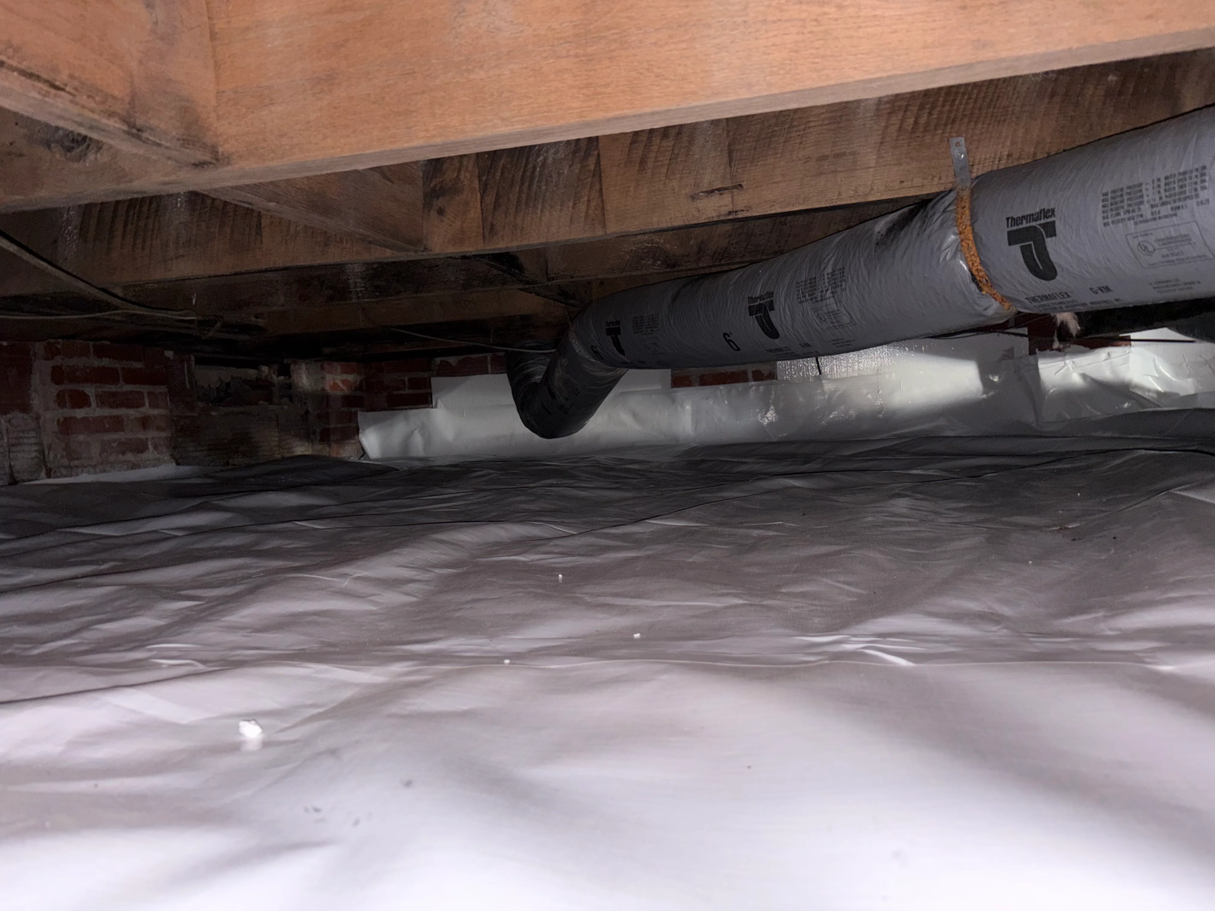 Crawl space with white vapor barrier, Thermafiber insulation, and wooden joists