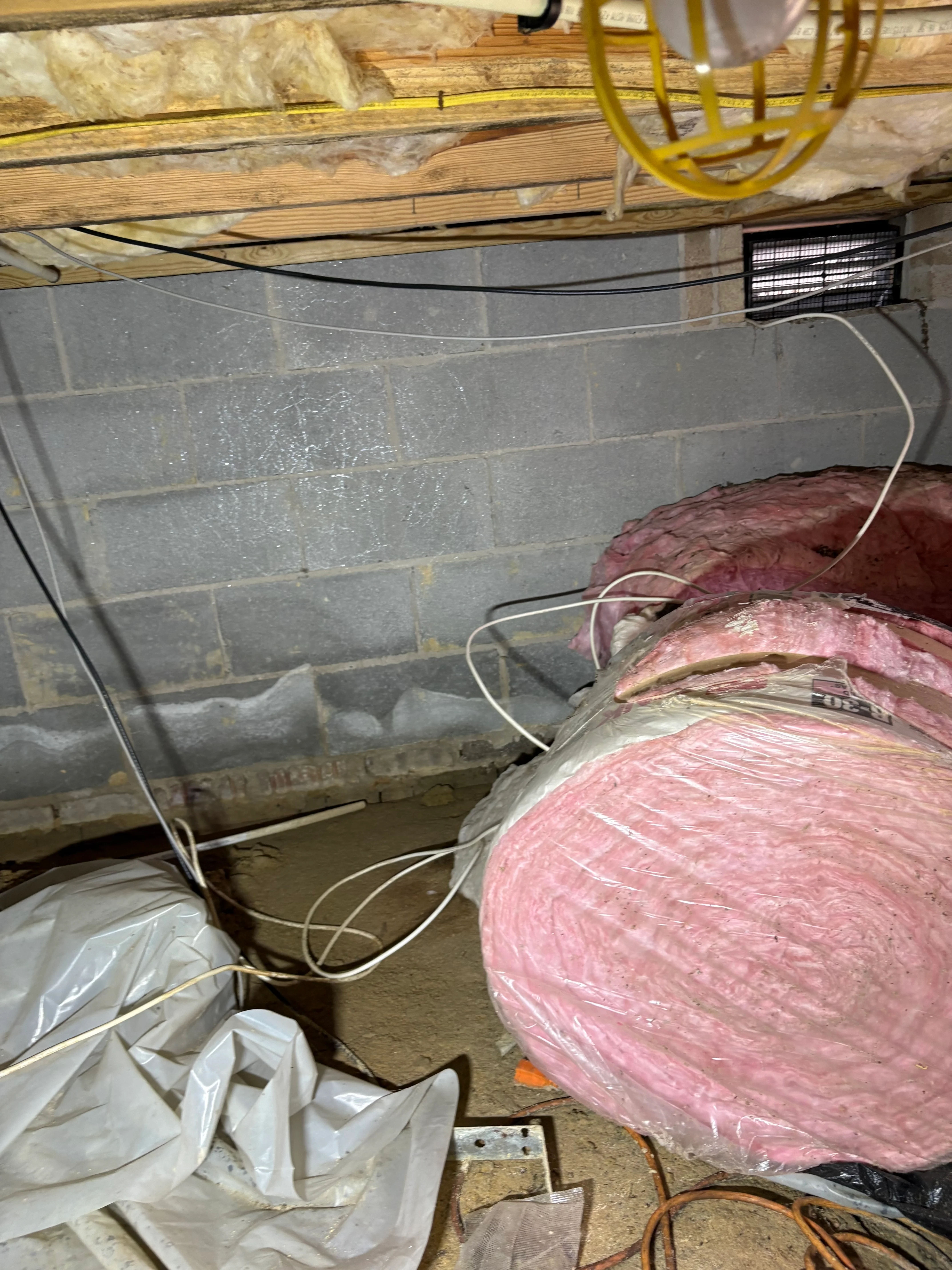 Pink fiberglass insulation batts installed in crawl space with concrete block foundation wall