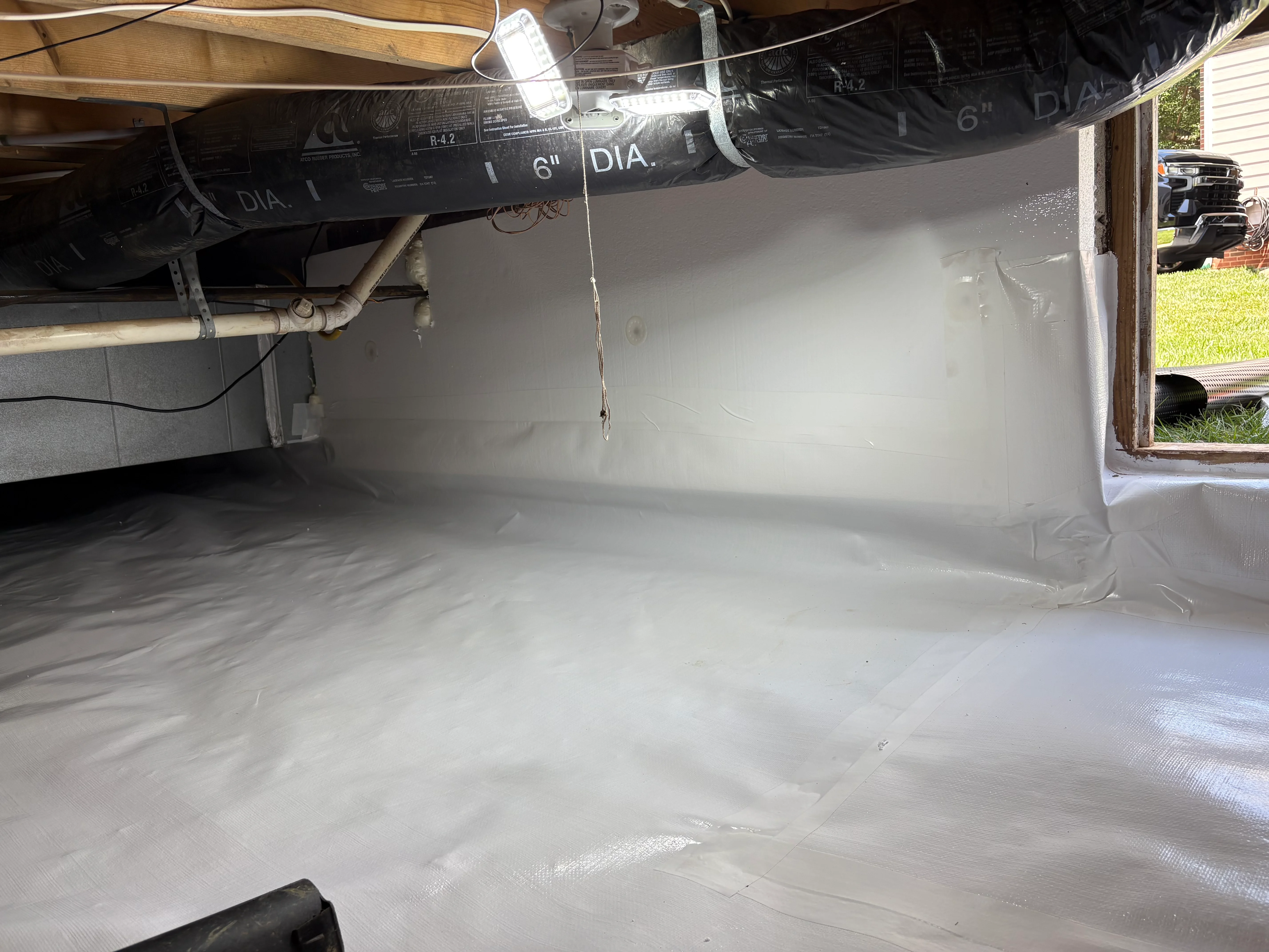 White vapor barrier installed in crawl space with ductwork and sealed seams