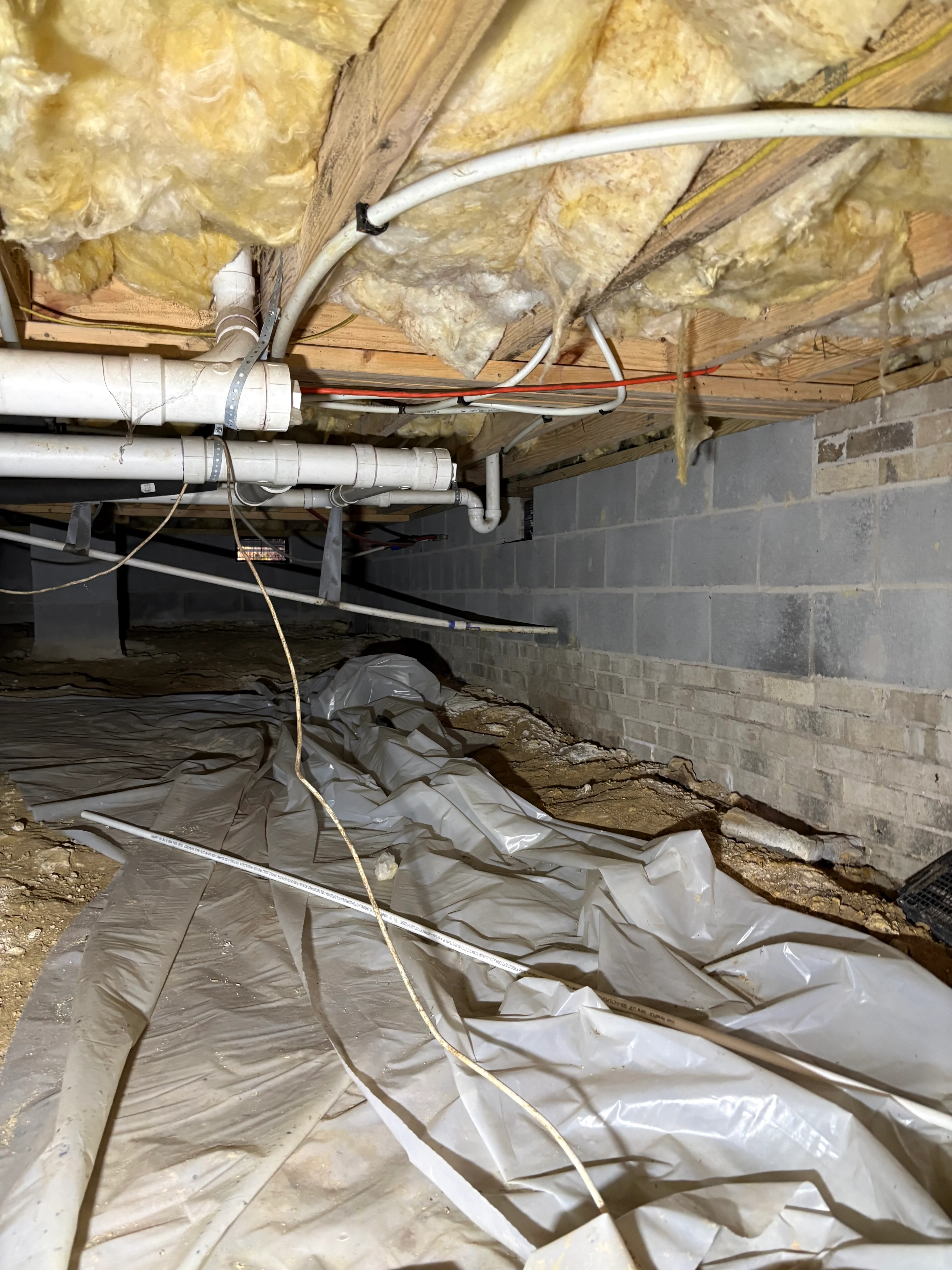 Crawl space with vapor barrier, insulation, and PVC piping installation