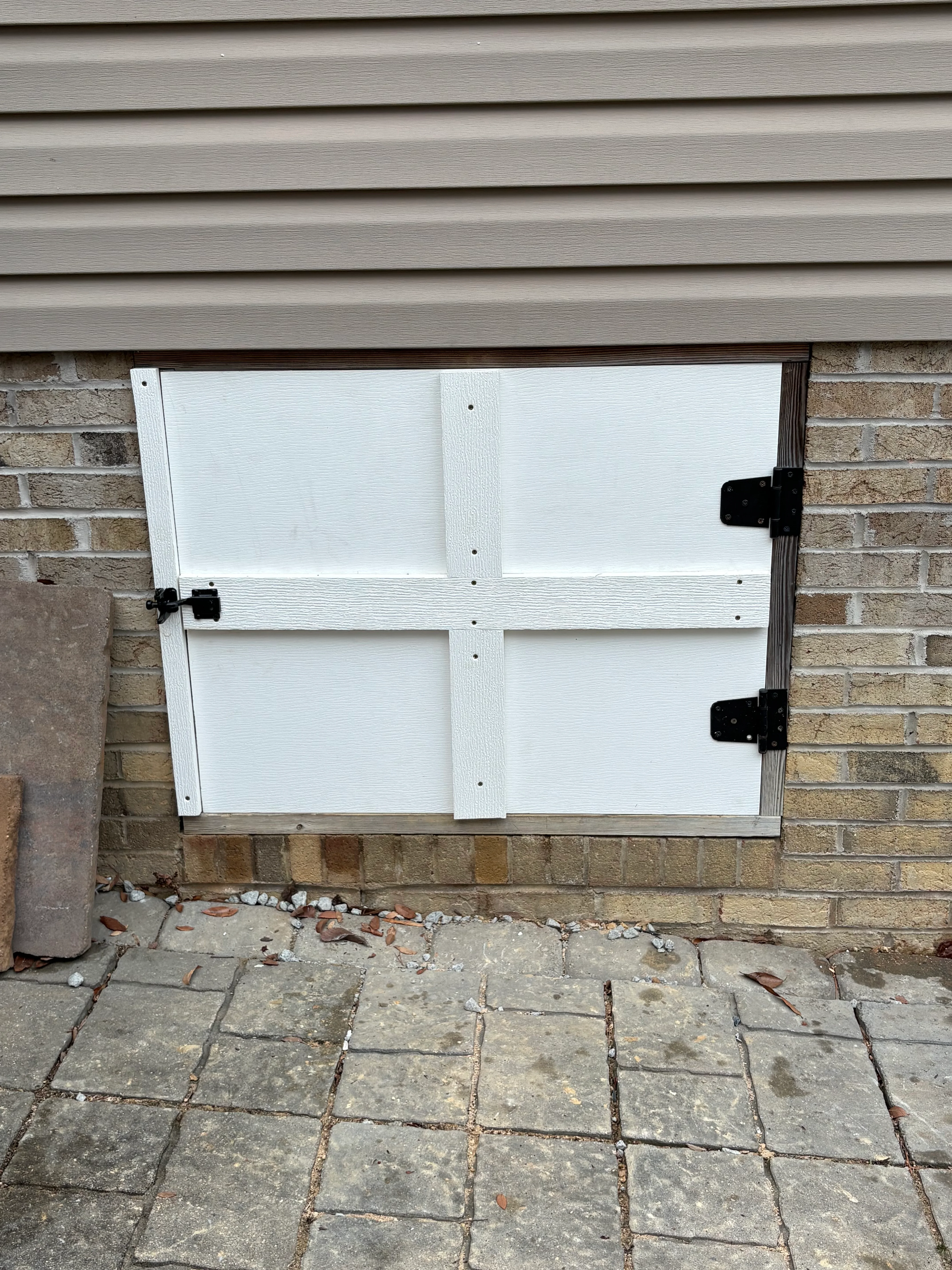 White crawl space access door with black hinges installed on brick foundation wall