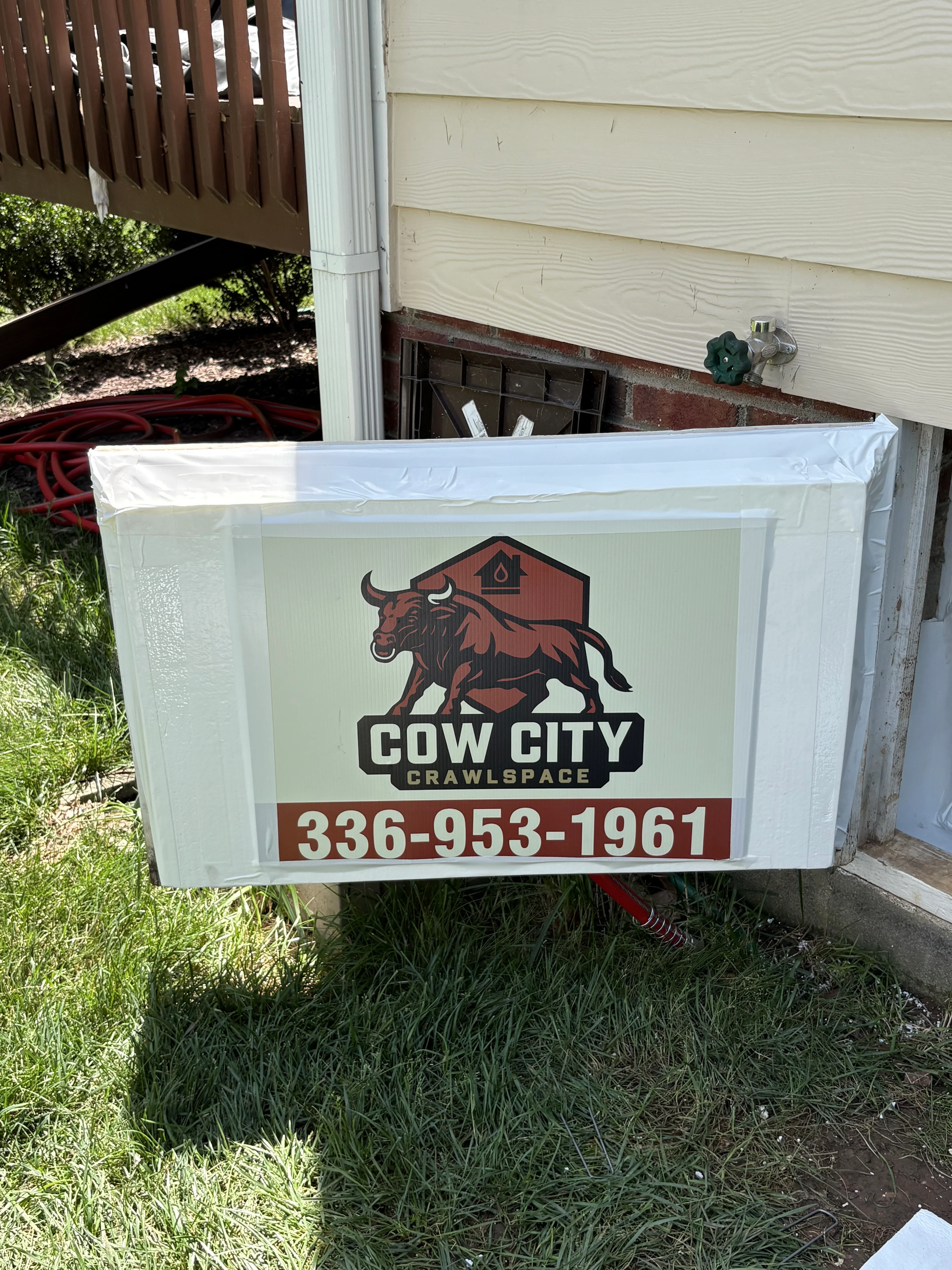 Cow City Crawlspace branded sign with bull logo mounted on residential foundation