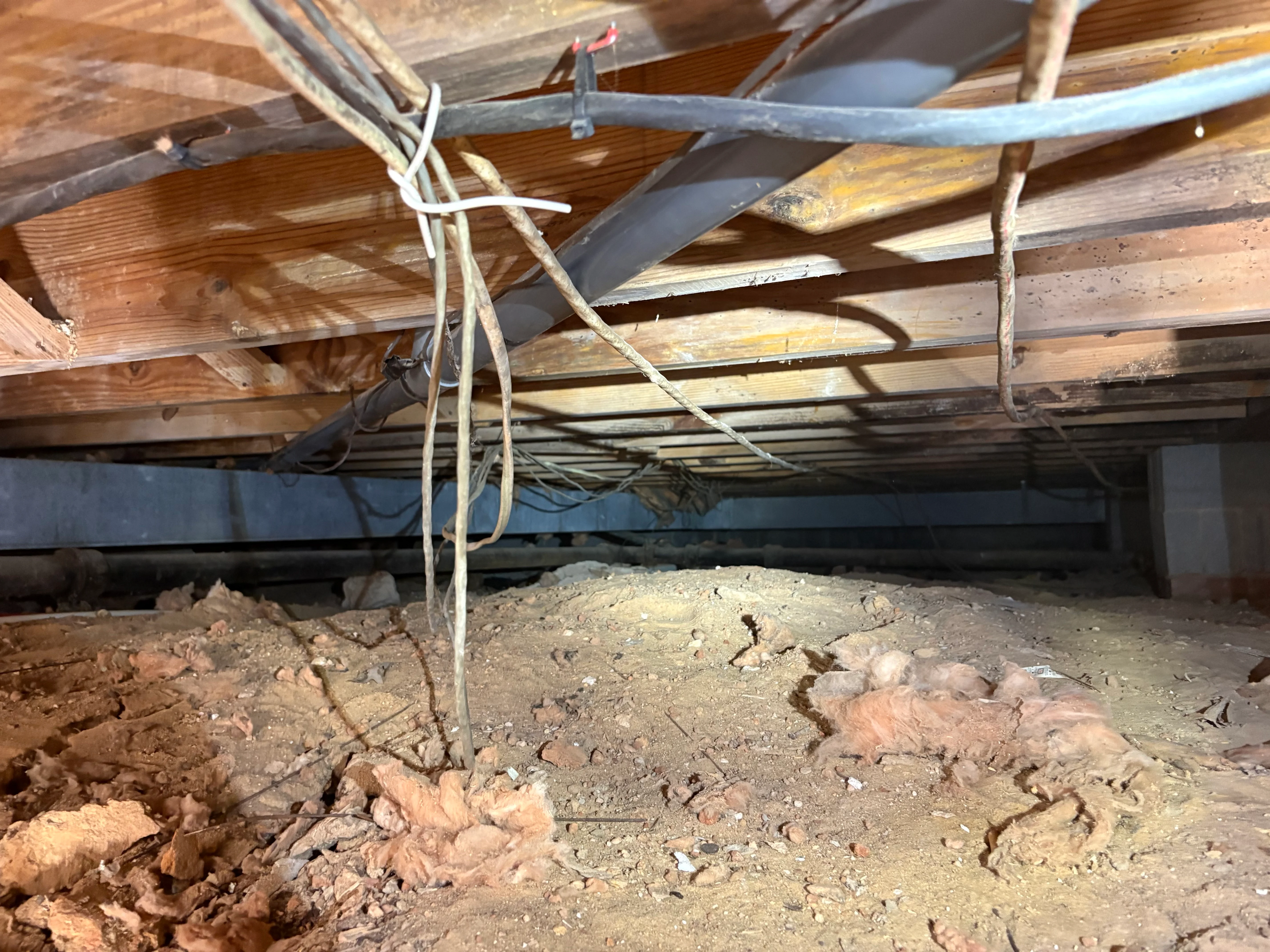 Crawl space interior showing damaged wooden joists, metal support straps, and exposed foundation elements