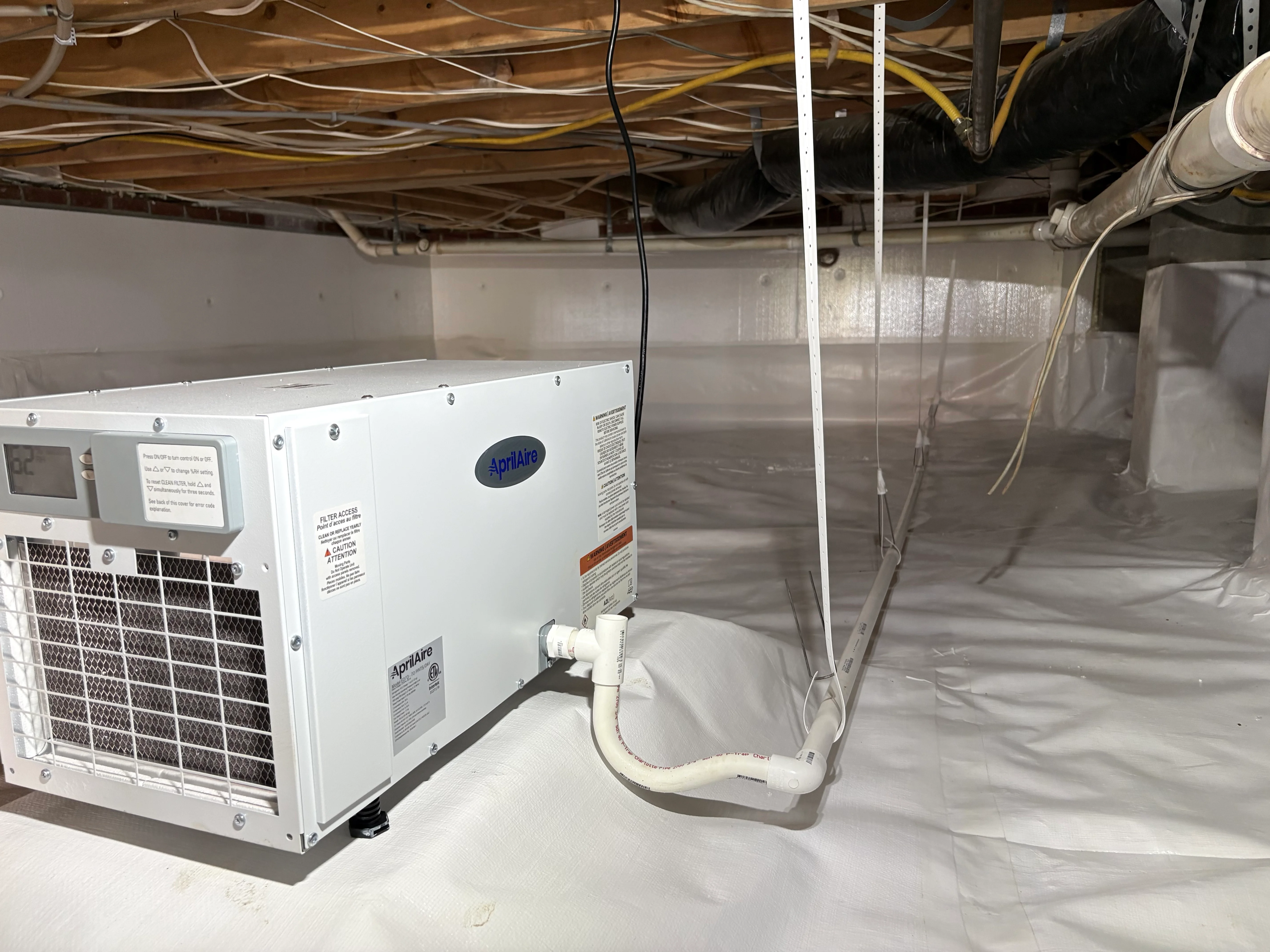 White dehumidifier unit installed in crawl space with connected drainage and ductwork