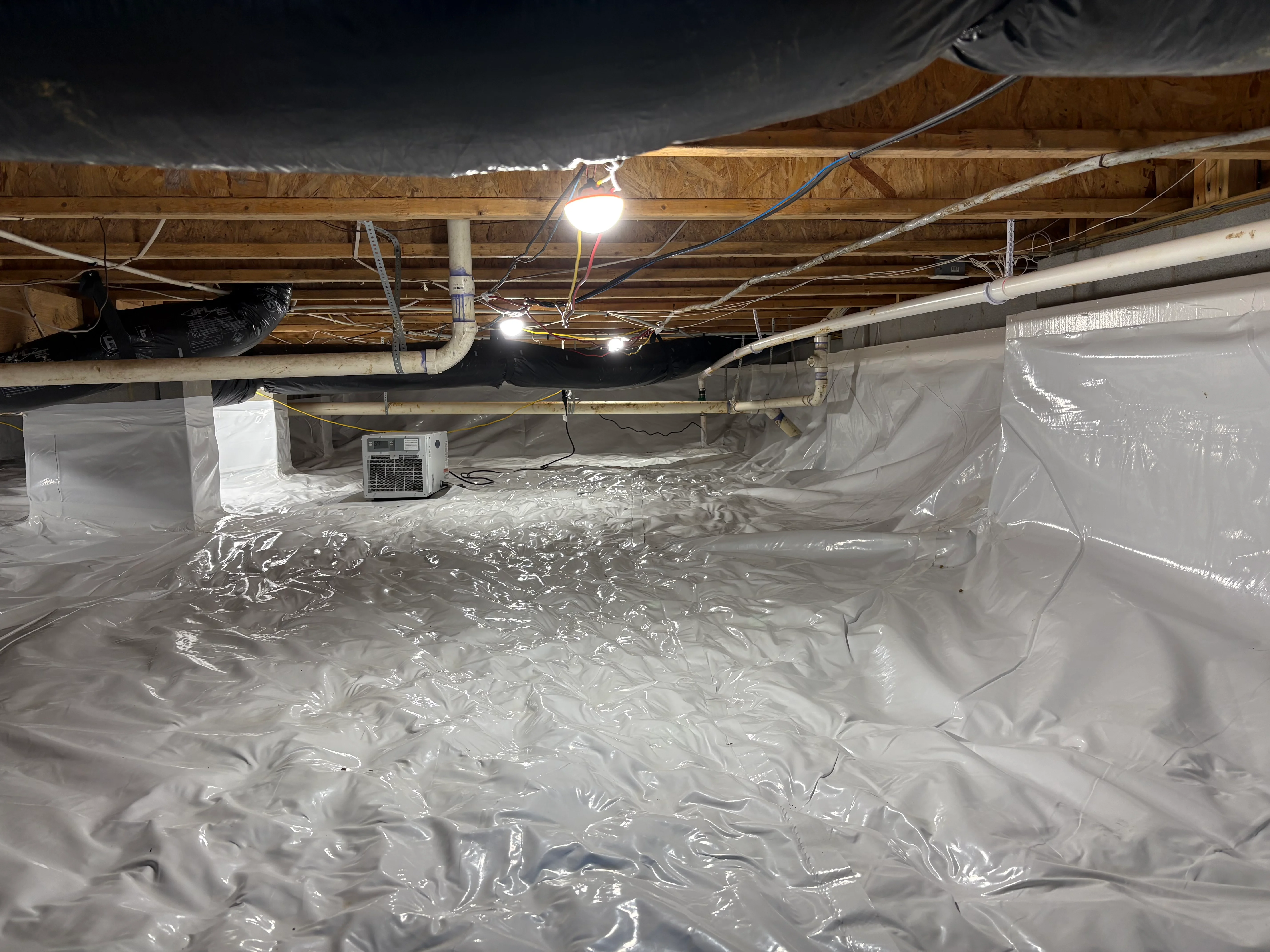 Crawl space with white polyethylene vapor barrier, dehumidifier unit, and LED lighting