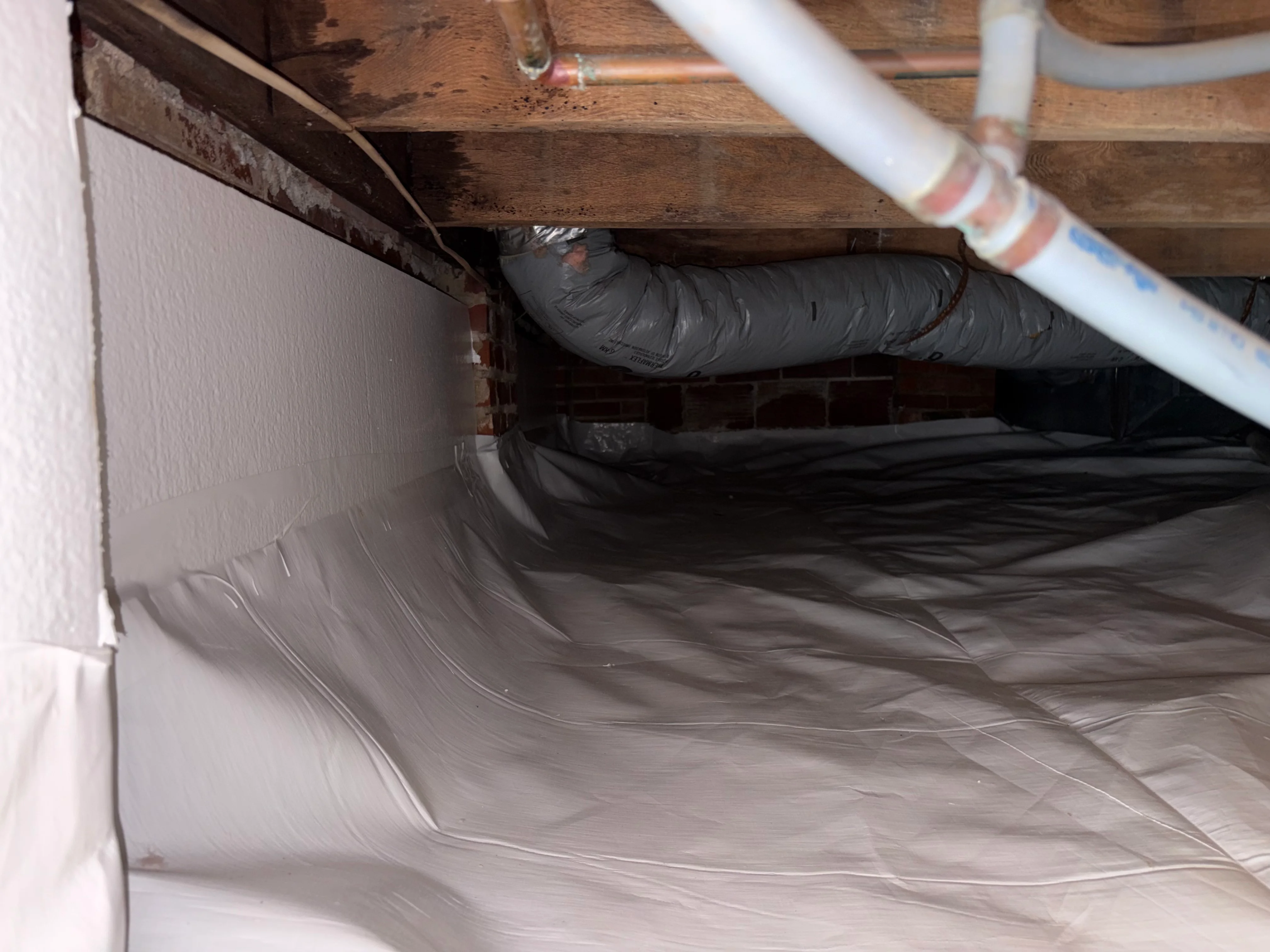 Crawl space with white vapor barrier and insulated black ductwork