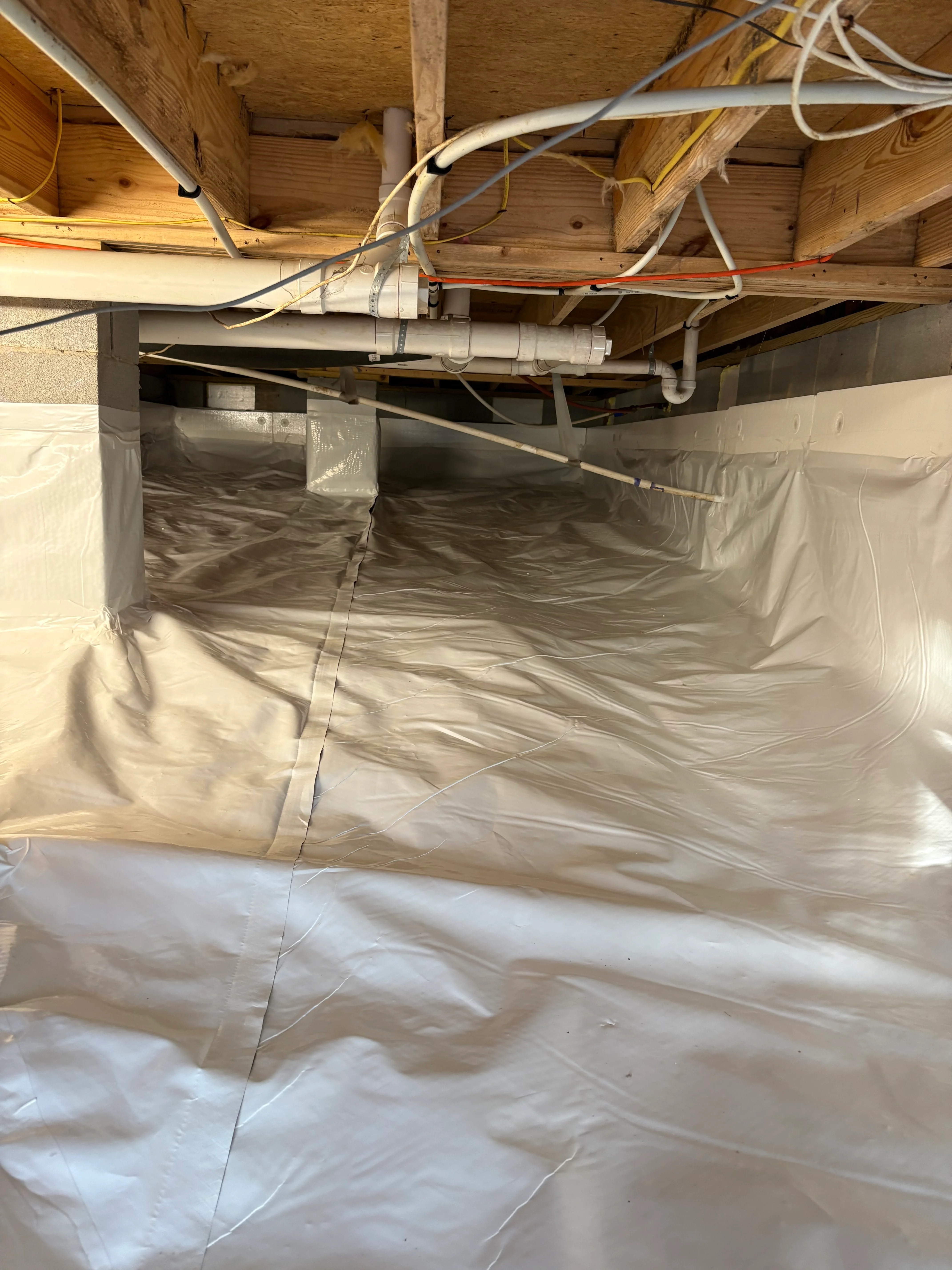 Crawl space with white vapor barrier encapsulation and PVC drainage pipes installed