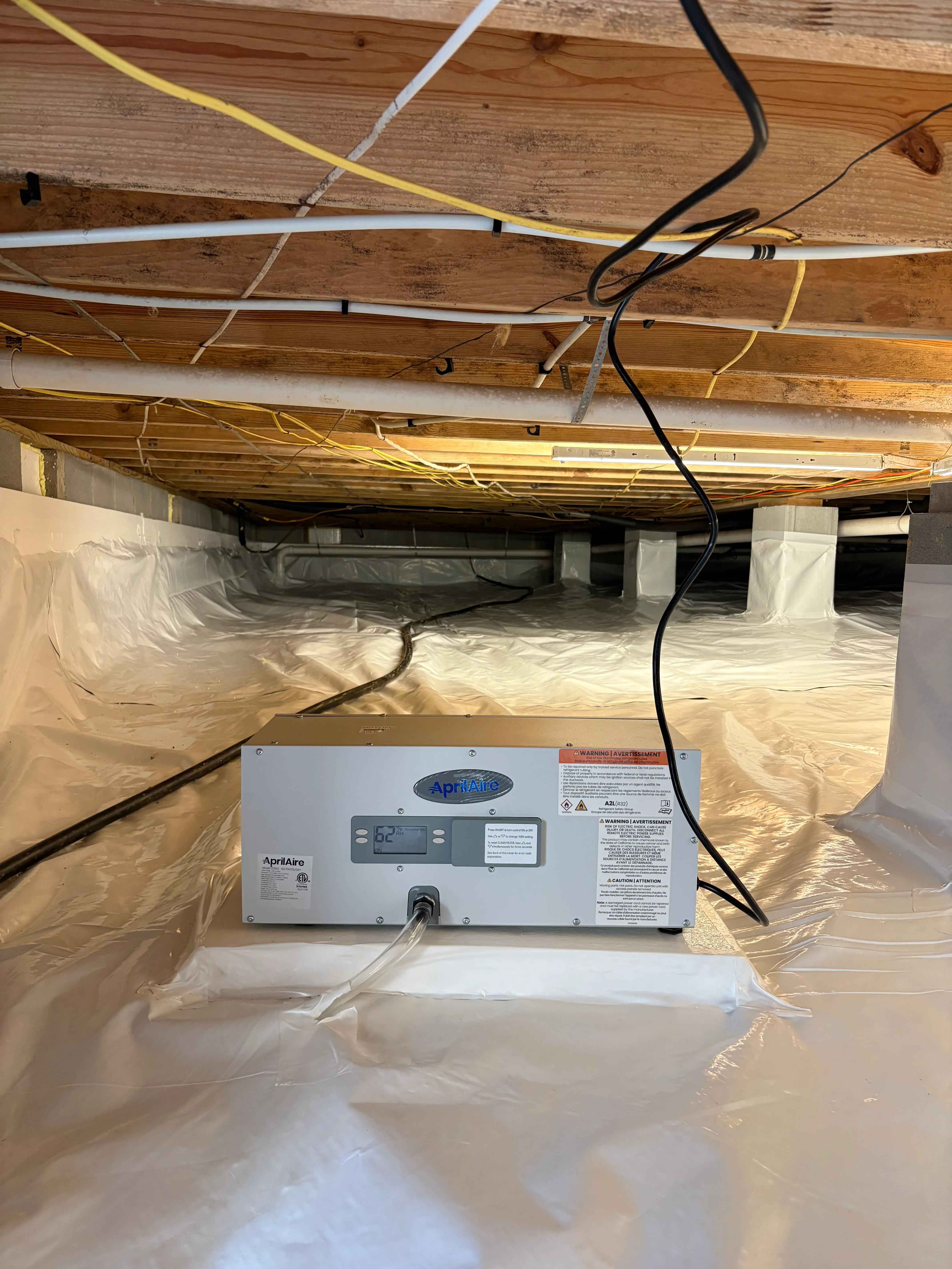 Crawl space with white vapor barrier, wooden joists, and AprilAire dehumidifier unit installed