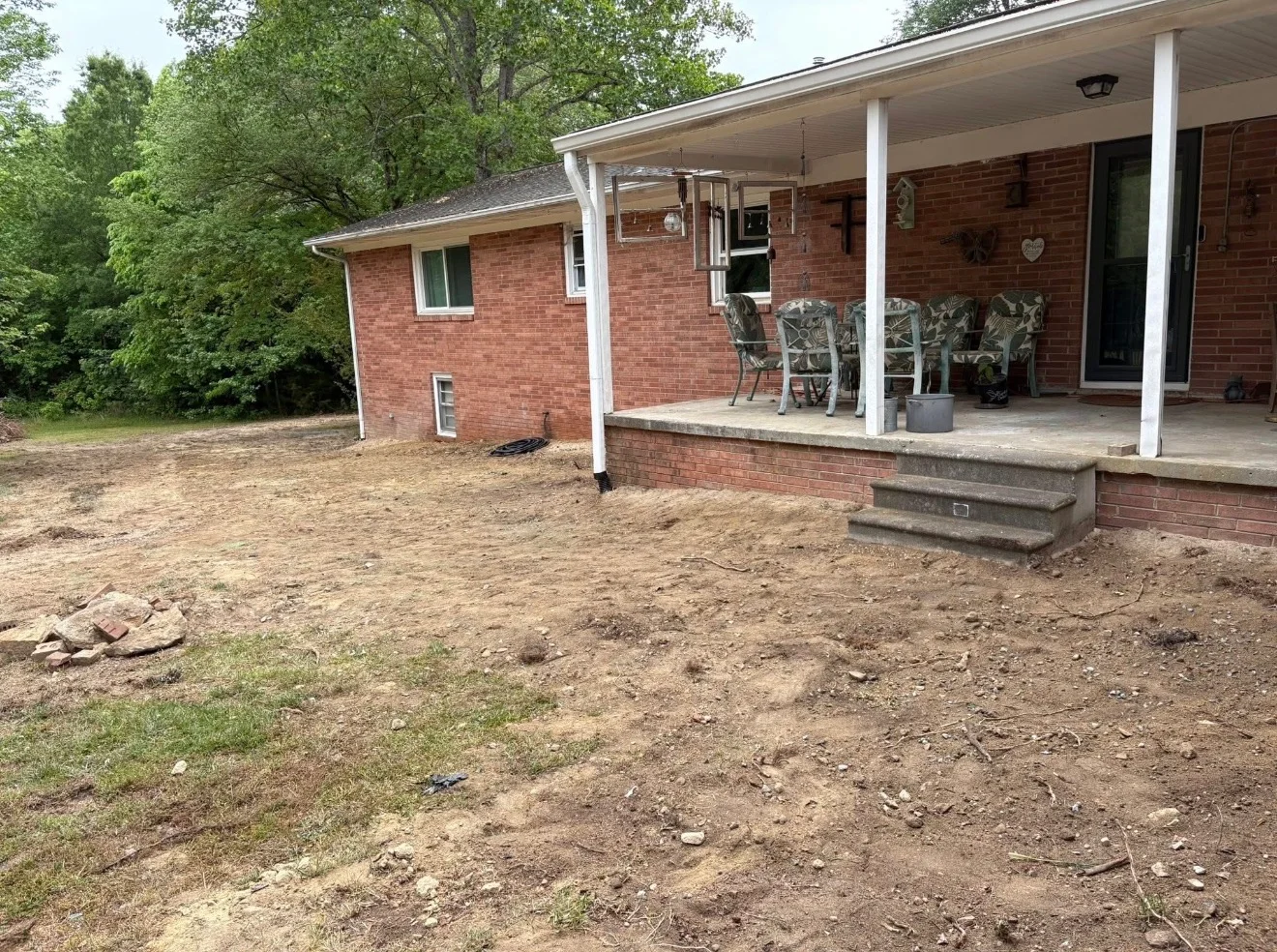 Excavated dirt yard area behind brick home with white porch columns and concrete foundation steps
