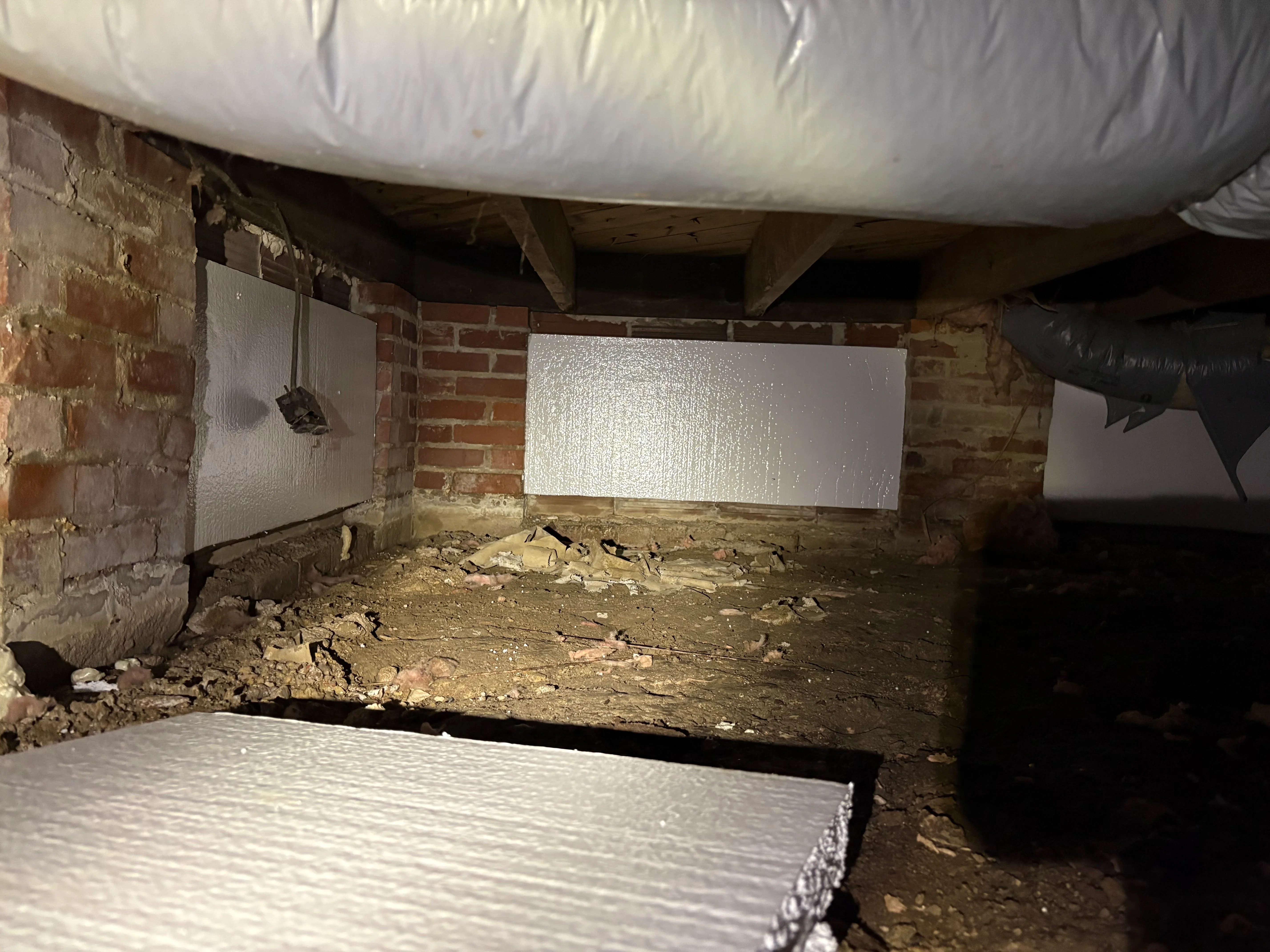 Crawl space with white vapor barrier on walls and ceiling, brick foundation visible
