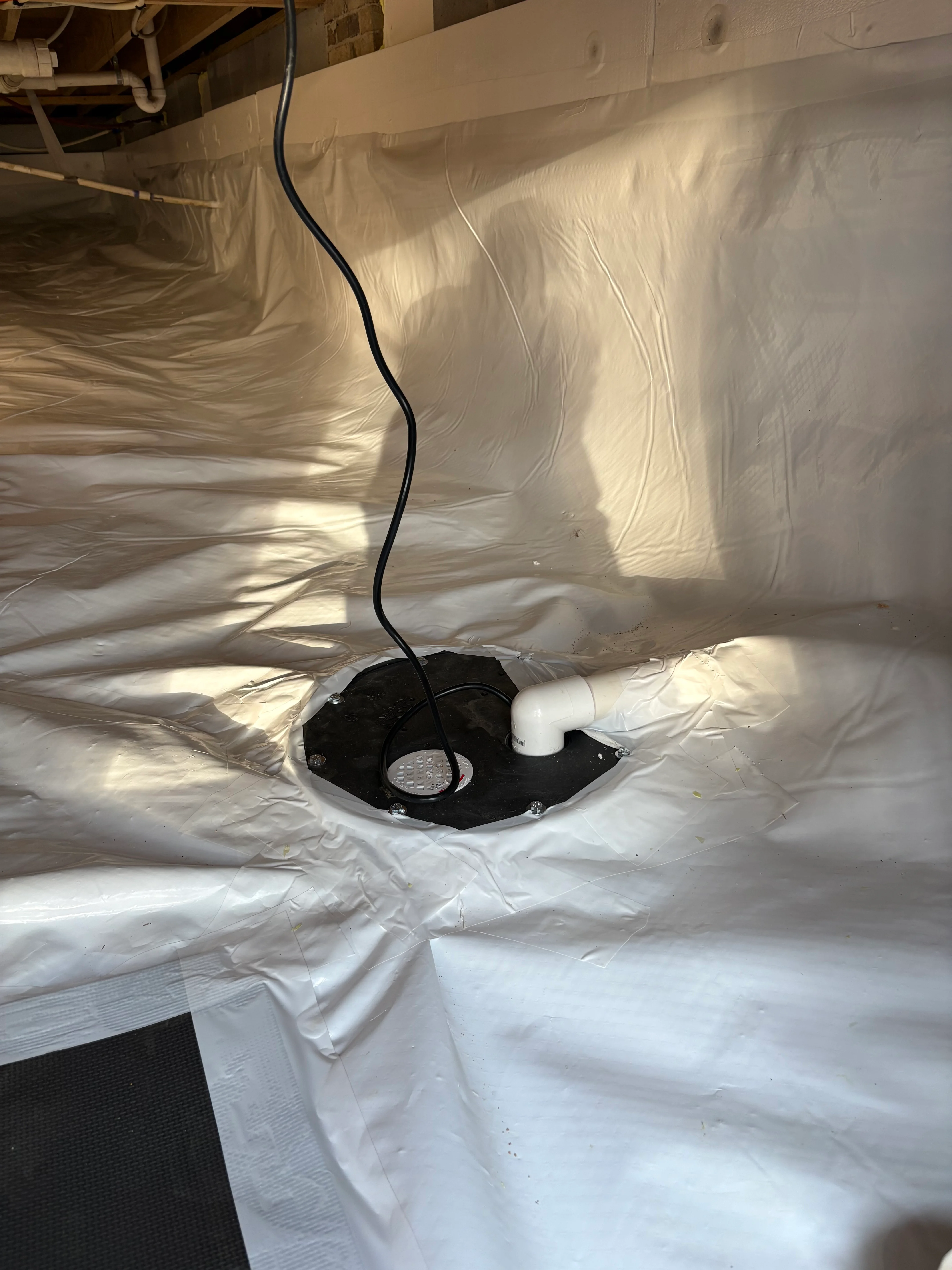 Crawl space with white vapor barrier and black drainage sump basin installation