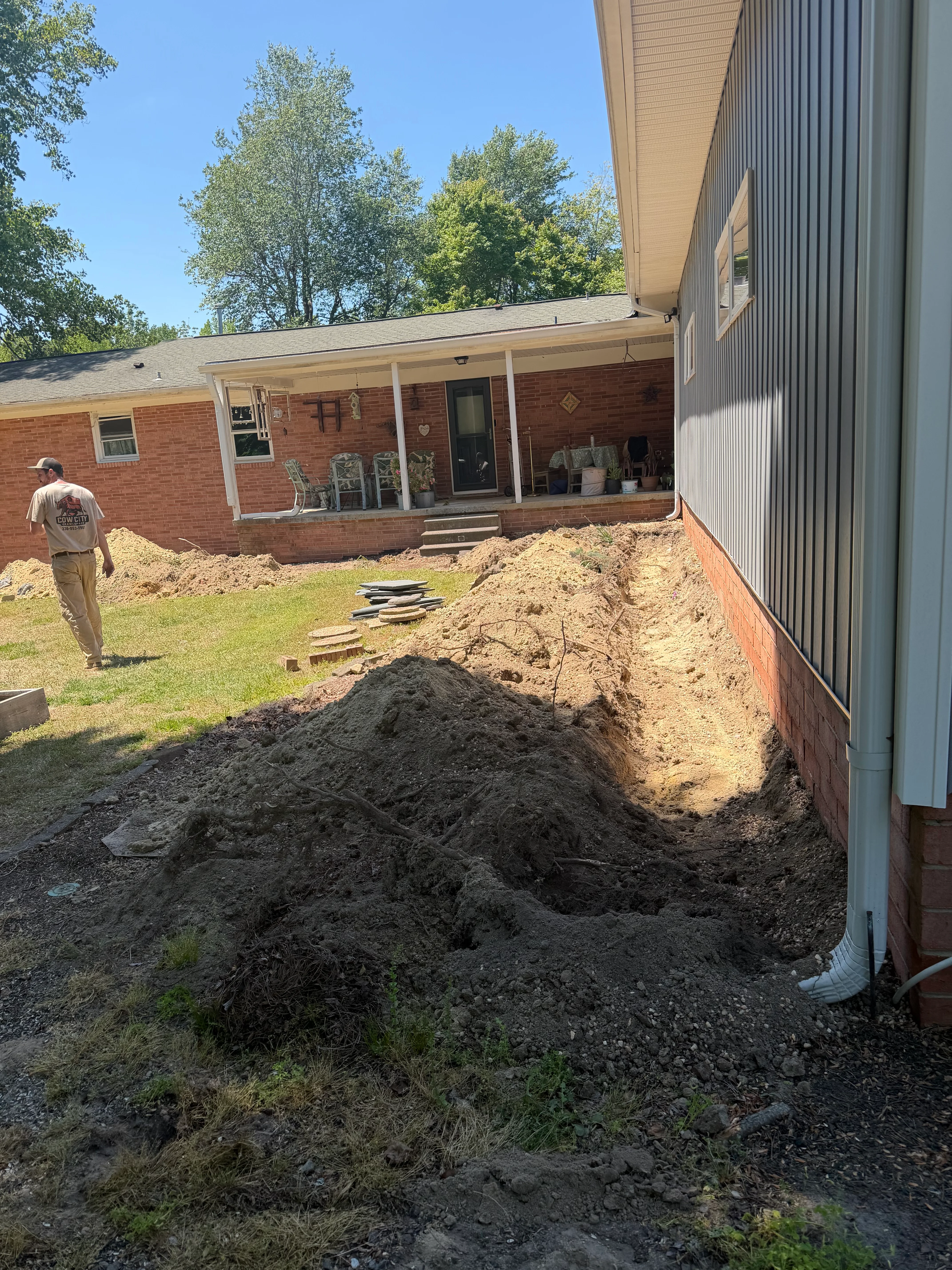 Excavated crawl space area beside brick home with soil piles and drainage line installation
