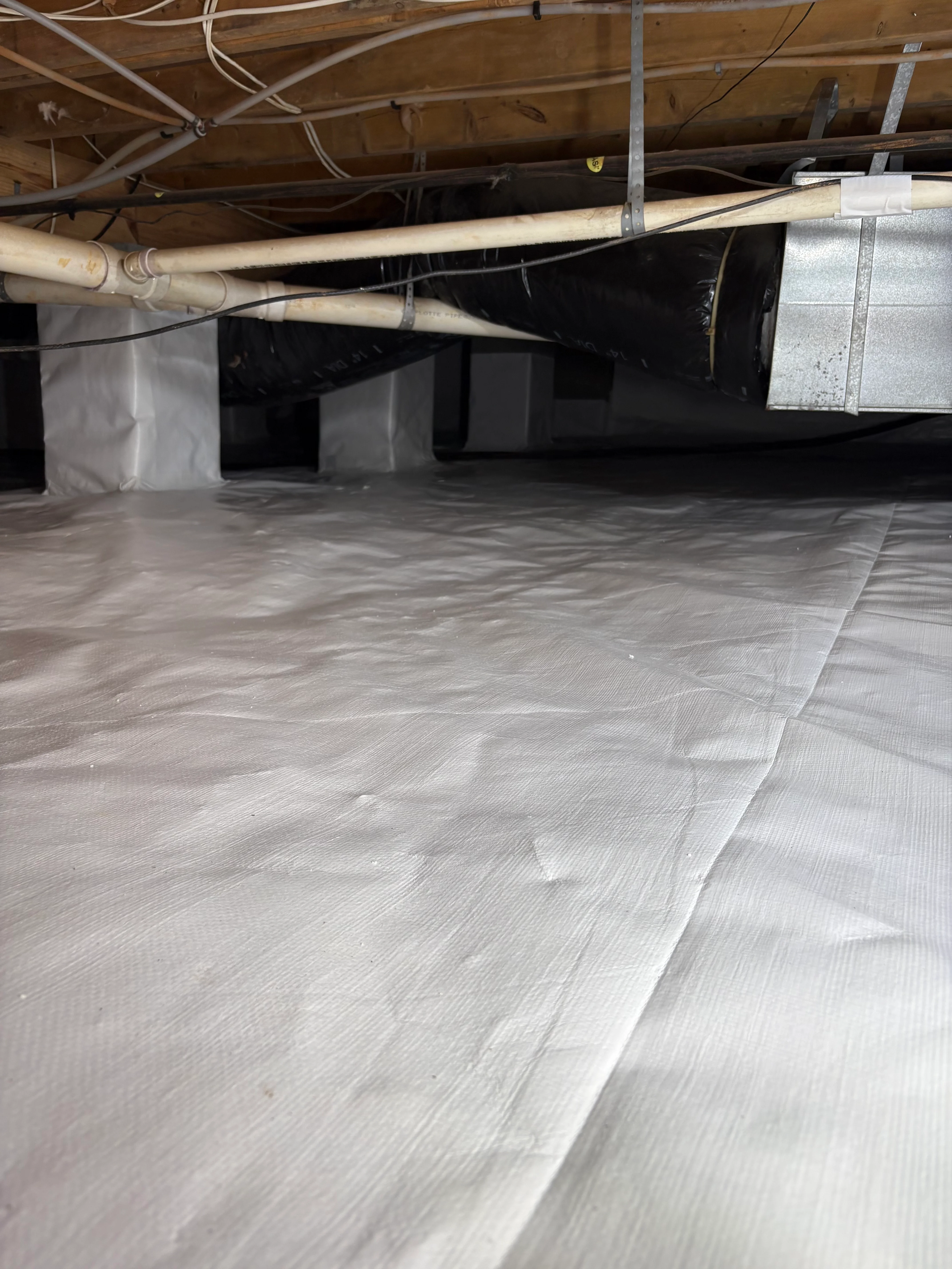 Crawl space with white vapor barrier, HVAC ducts, and support posts installed